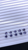May include: Eight pear-shaped purple gemstones on a white surface with a textured pattern.